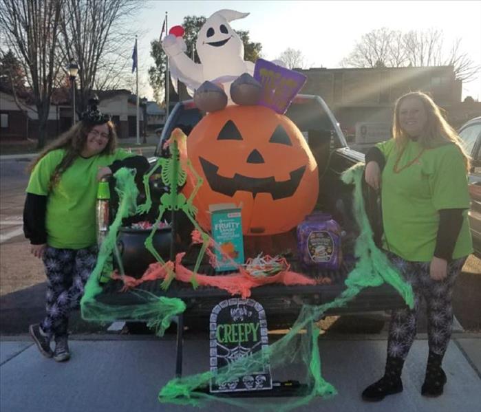 Two women on either side of the back of a truck that is decorated with spider webs and a blow-up pumpkin and ghost