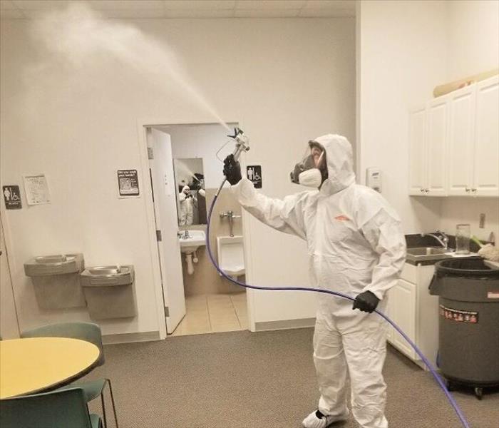 man wearing PPE and spraying room