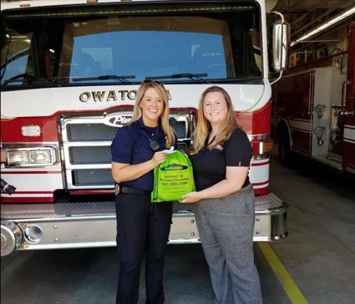 Two women standing in front of a fire truck holding a green SERVPRO bag.